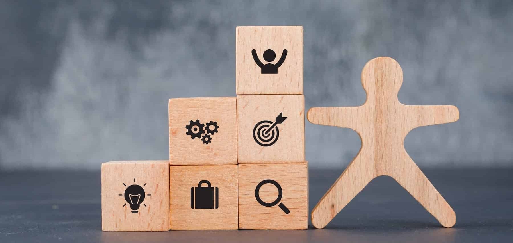 il bilancio di competenze: giochi in legno a forma di persone e blocchi con icone relative alla crescita e alla soddisfazione personale e lavorativa