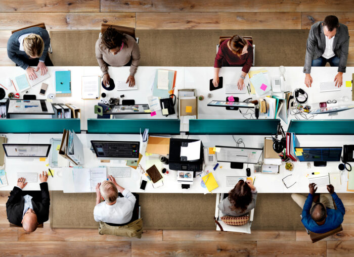 persone che lavorano in un ufficio open space davanti a schermi pc