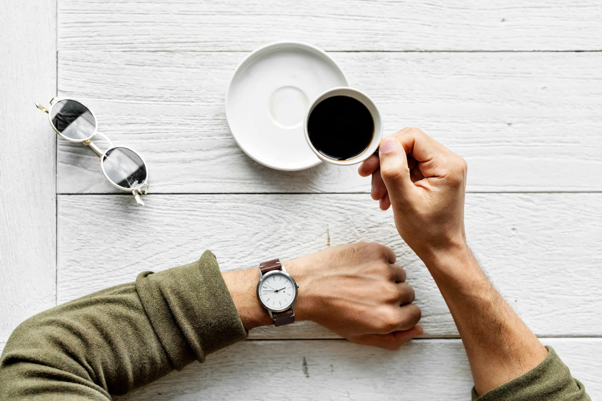 primo piano di mani di uomo con orologio sul polso e tazza del caffè