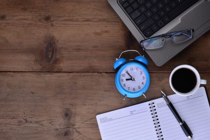 scrivania con agenda, pc e orologio blu a rappresentare il momento di pausa lavorativa