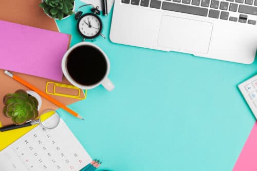 primo piano di scrivania celeste con pc, post-it, tazzina del caffè e altri oggetti