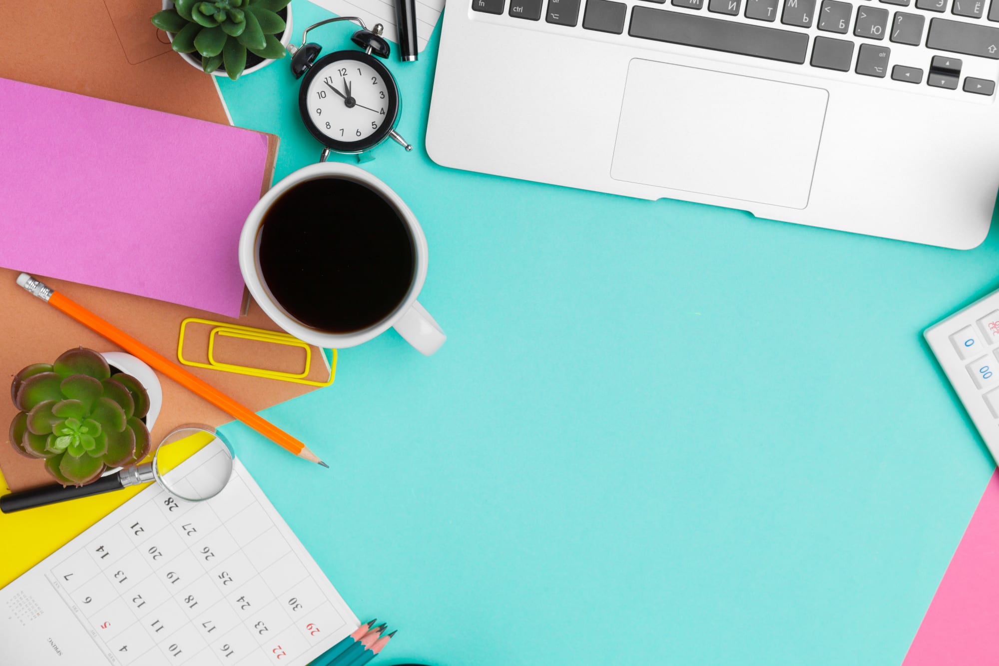 primo piano di scrivania celeste con pc, post-it, tazzina del caffè e altri oggetti