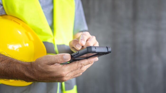 operaio con giacca catarifrangente e casco di sicurezza che timbra il cartellino dall'app aziendale con un sistema di timbratura virtuale