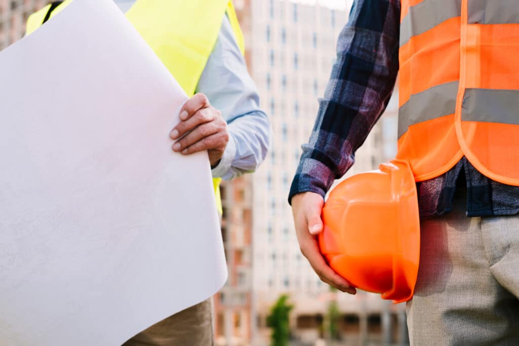 operai in cantiere: uno consulta i piani di costruzione e l'altro sostiene il caschetto di sicurezza