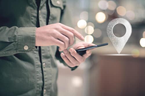 primo piano di persona che clicca sullo schermo del proprio smartphone e icona di geolocalizzazione per la timbratura geolocalizzata